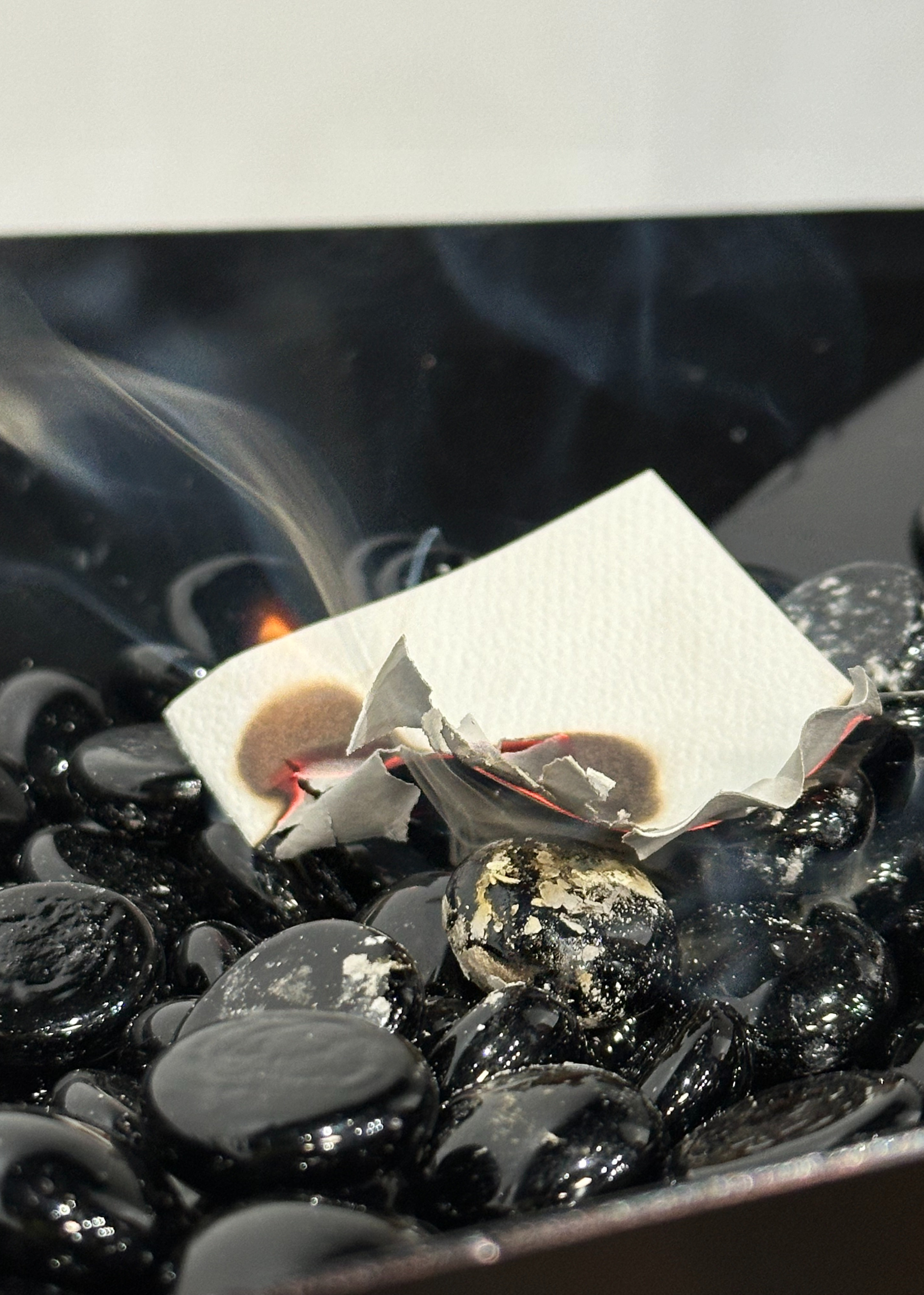 A close-up of a burner bowl with pebbles and a burning paper