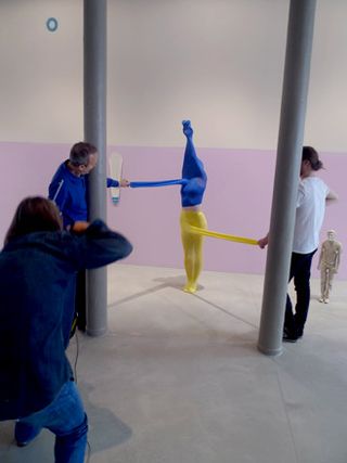 A model with both legs in one leg of a pair of yellow tights, and arms and head in one leg of a pair of blue tights