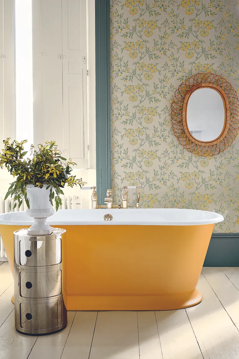 bathroom with yellow painted bath, wallpaper with yellow floral design, wicker mirror, metal storage