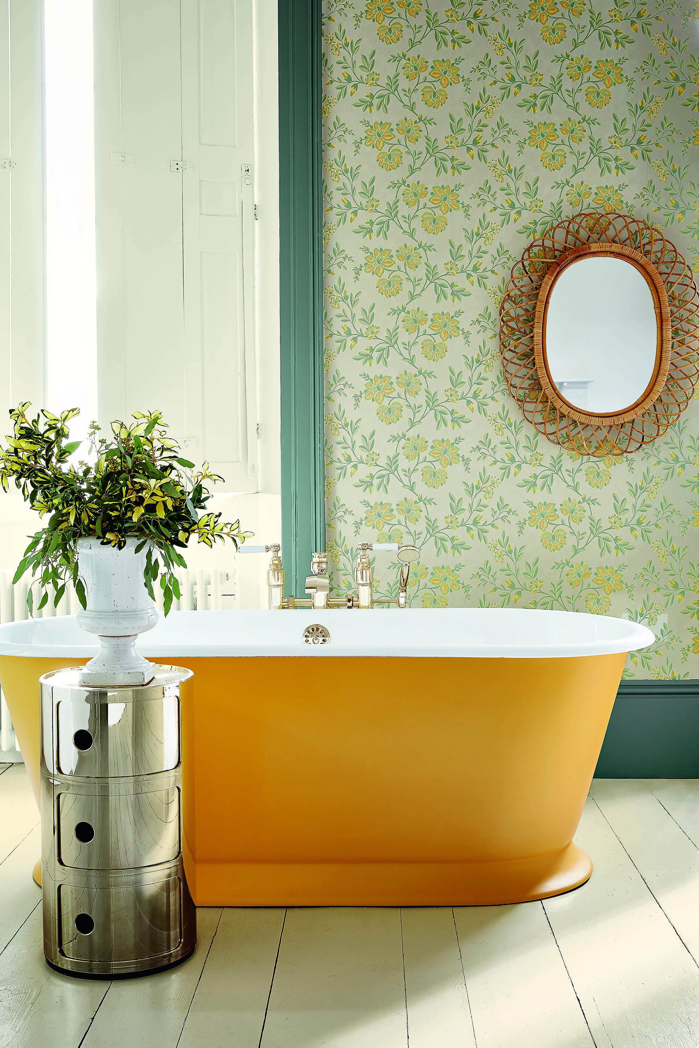 bathroom with yellow painted bath, wallpaper with yellow floral design, wicker mirror, metal storage