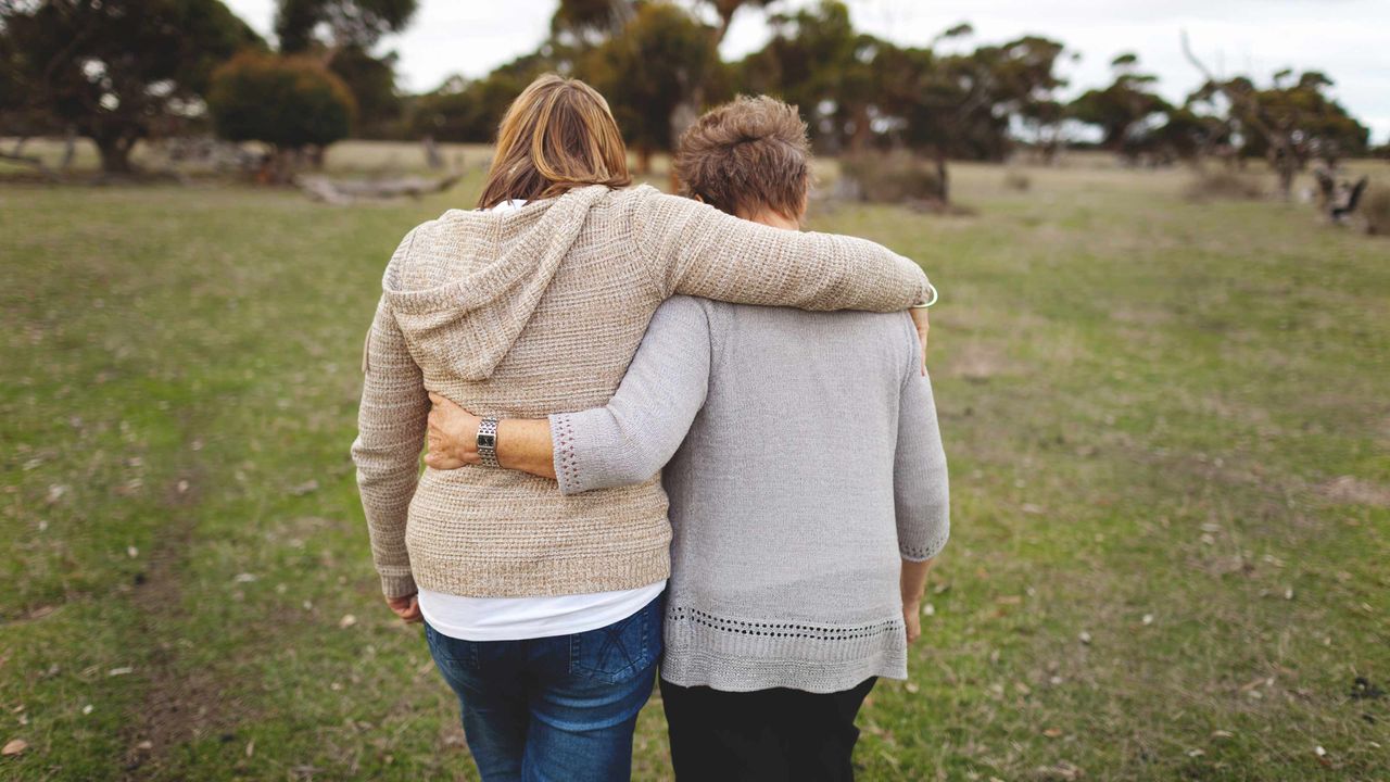 An adult daughter walks with her arm over her mom&amp;#039;s shoulder.