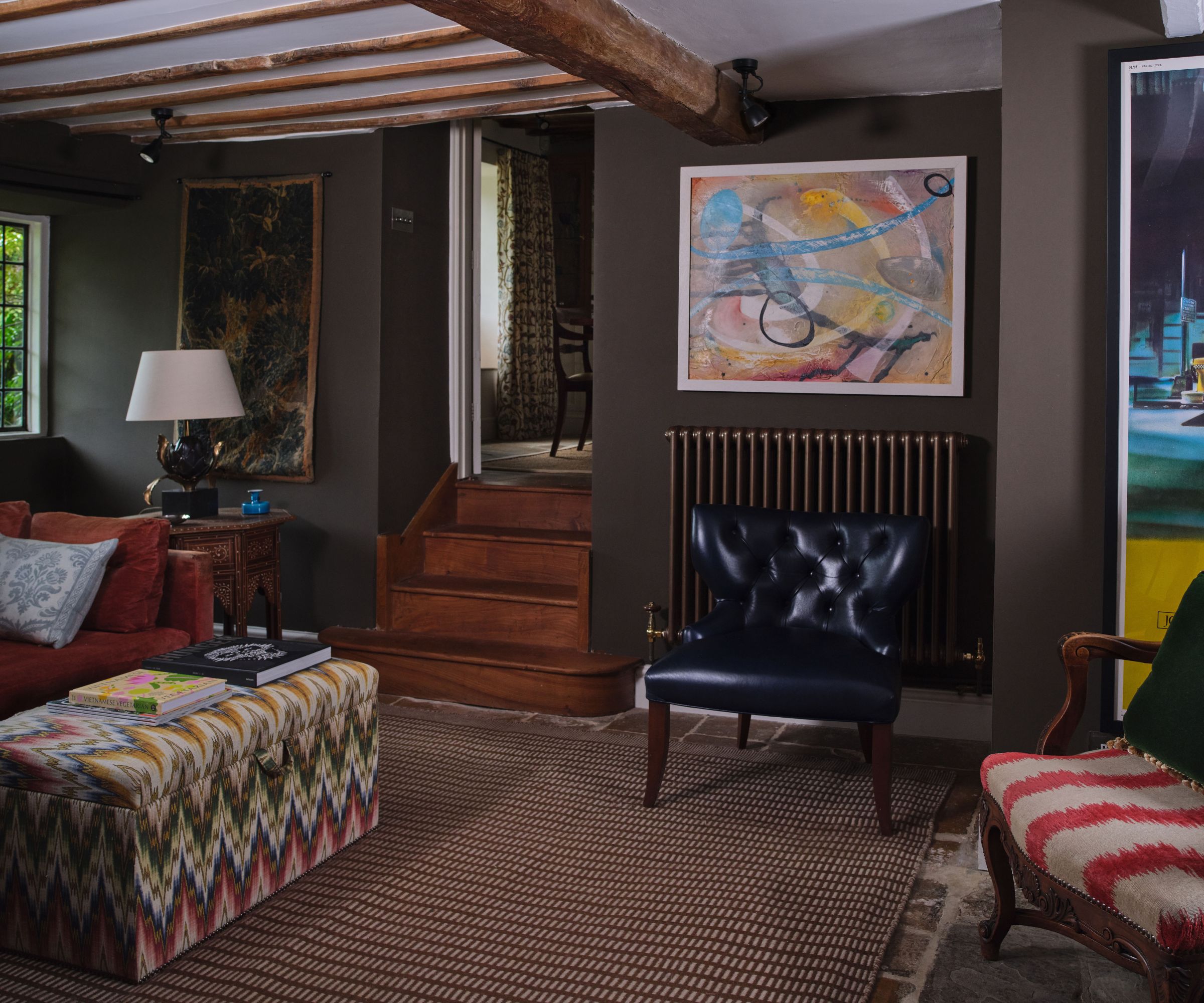 A cottage living room decorated with antique furniture, moody colors, and modern art