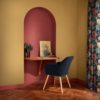 A room painted in a mustard yellow with a deep red alcove with a built in desk