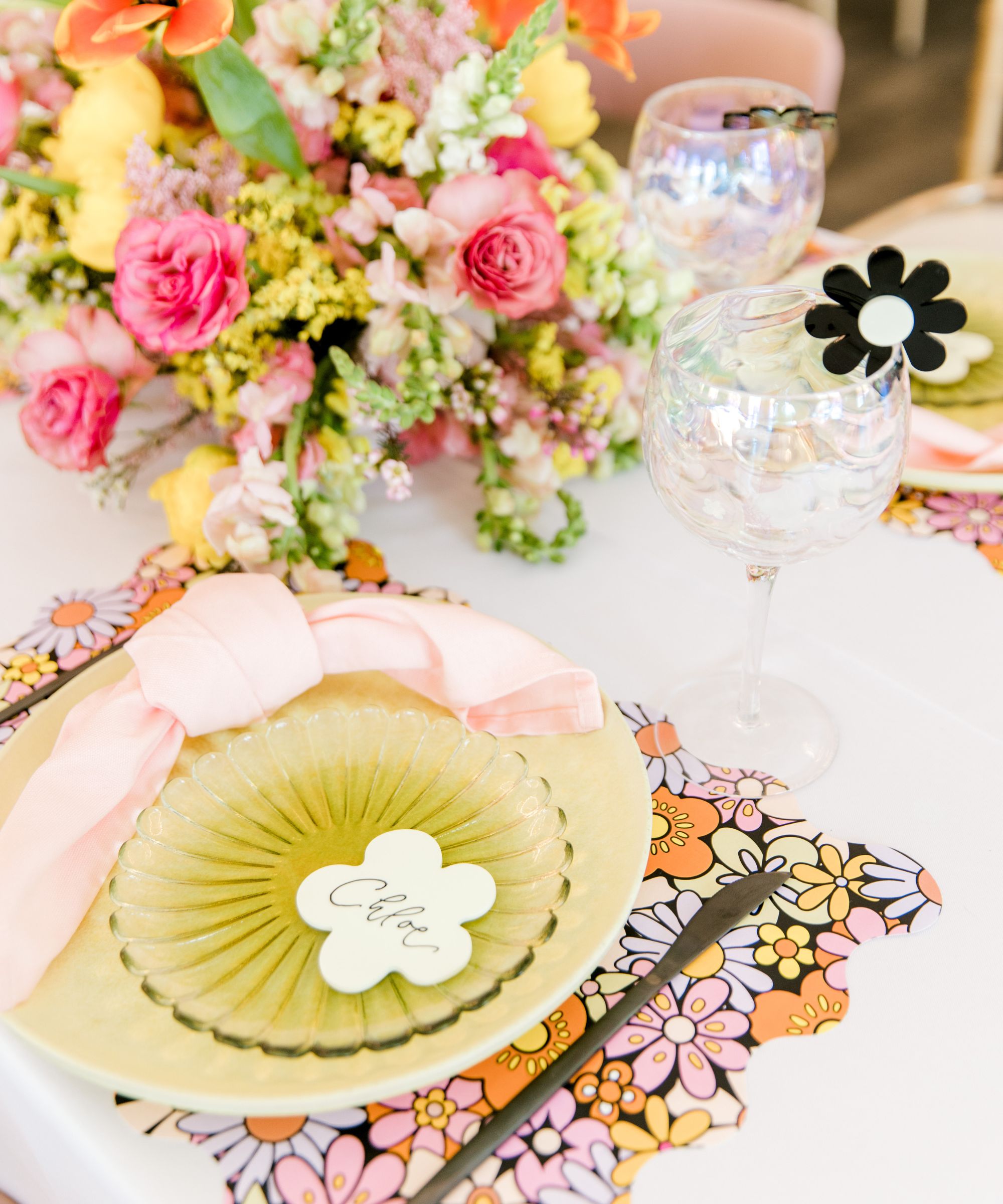 bright pink and orange themed tablescape with bold floral placemats, yellow plates, pink napkins and colorful flowers