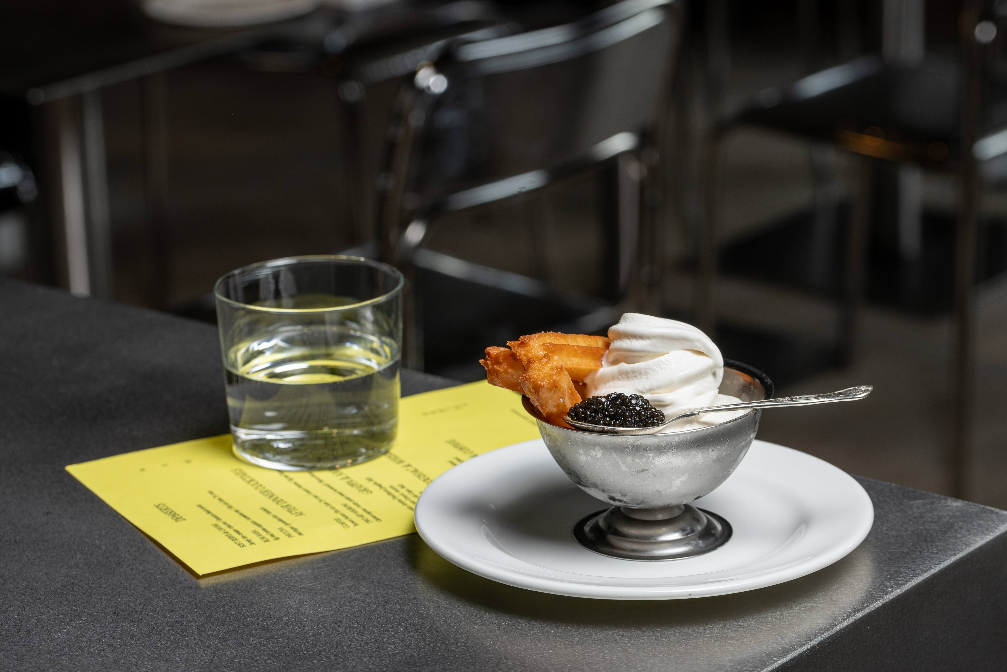 A series of beautifully presented, colorful restaurant plates and cocktails come served in white or chrome tableware and are placed atop silver tables.