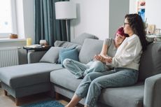 A mom holds her teen daughter sitting on a couch.