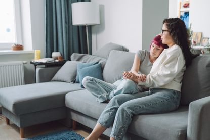 A mom holds her teen daughter sitting on a couch.