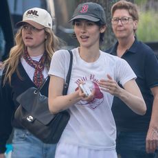 Gracie wears a baseball cap, white graphic tee, and a black chanel bag.