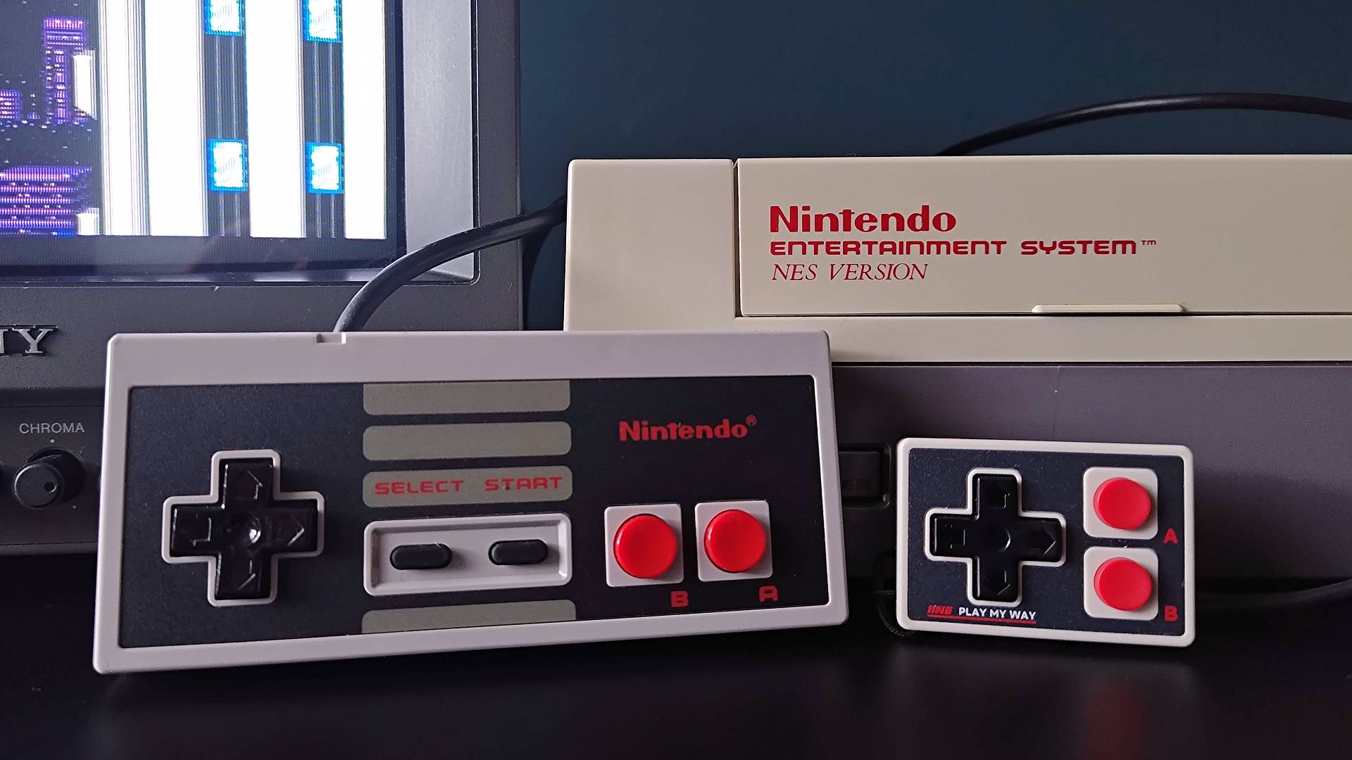 IINE Gamebrick Mini controller next to NES and controller with Sony Trinitron PVM CRT on left and Mega Man 2 intro on screen.