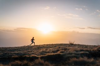 A man running across a grassy landscape with the sun setting in the background