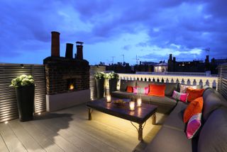 Roof garden with soft lighting by John Cullen Lighting, and a corner sofa,dining table and brick fireplace