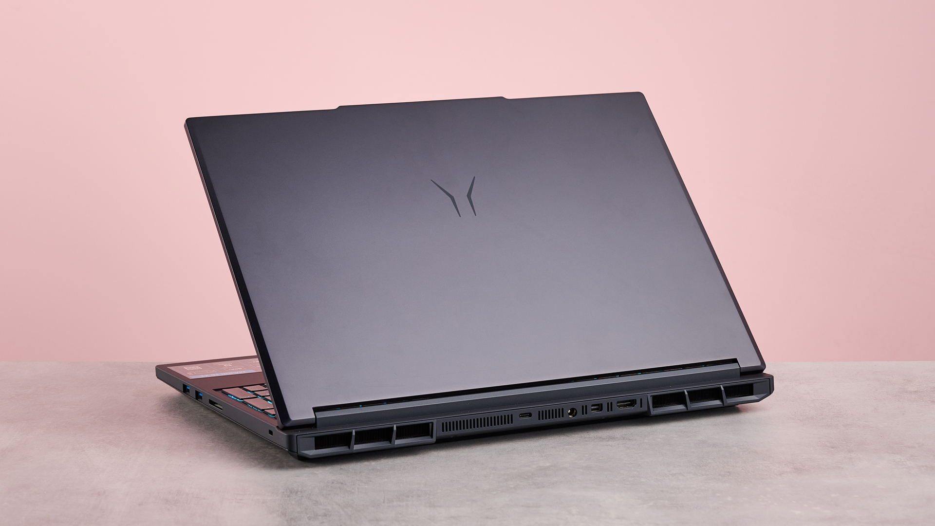 Back three-quarter view of Medion Erazer Major 16 X1, open on desk with pink wall in background