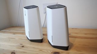 Två stycken Netgear Orbi Pro WiFi 6 står placerade på ett träbord mot en vit bakgrund.