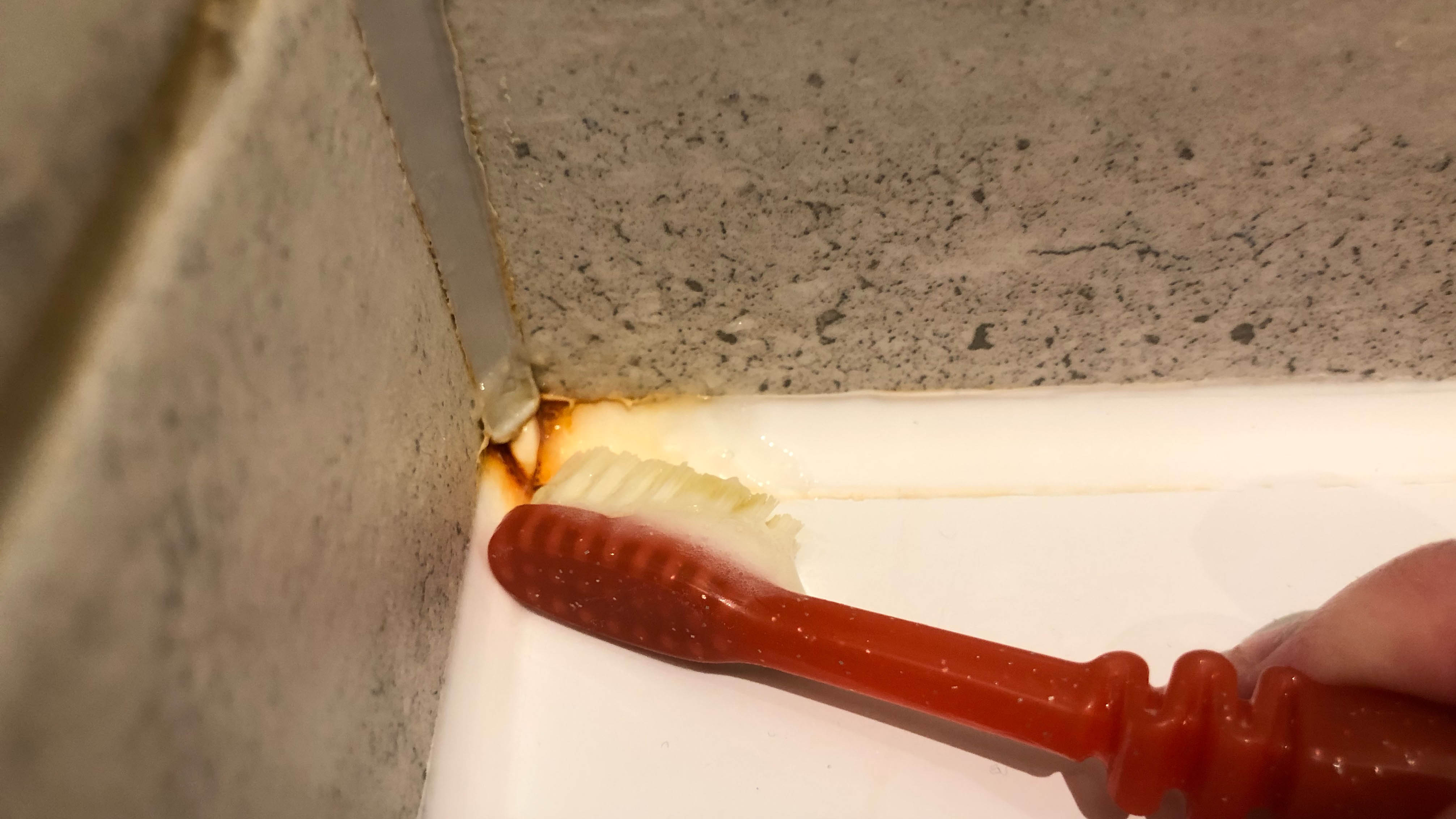 A toothbrush cleaning the sealant in the shower with toothpaste