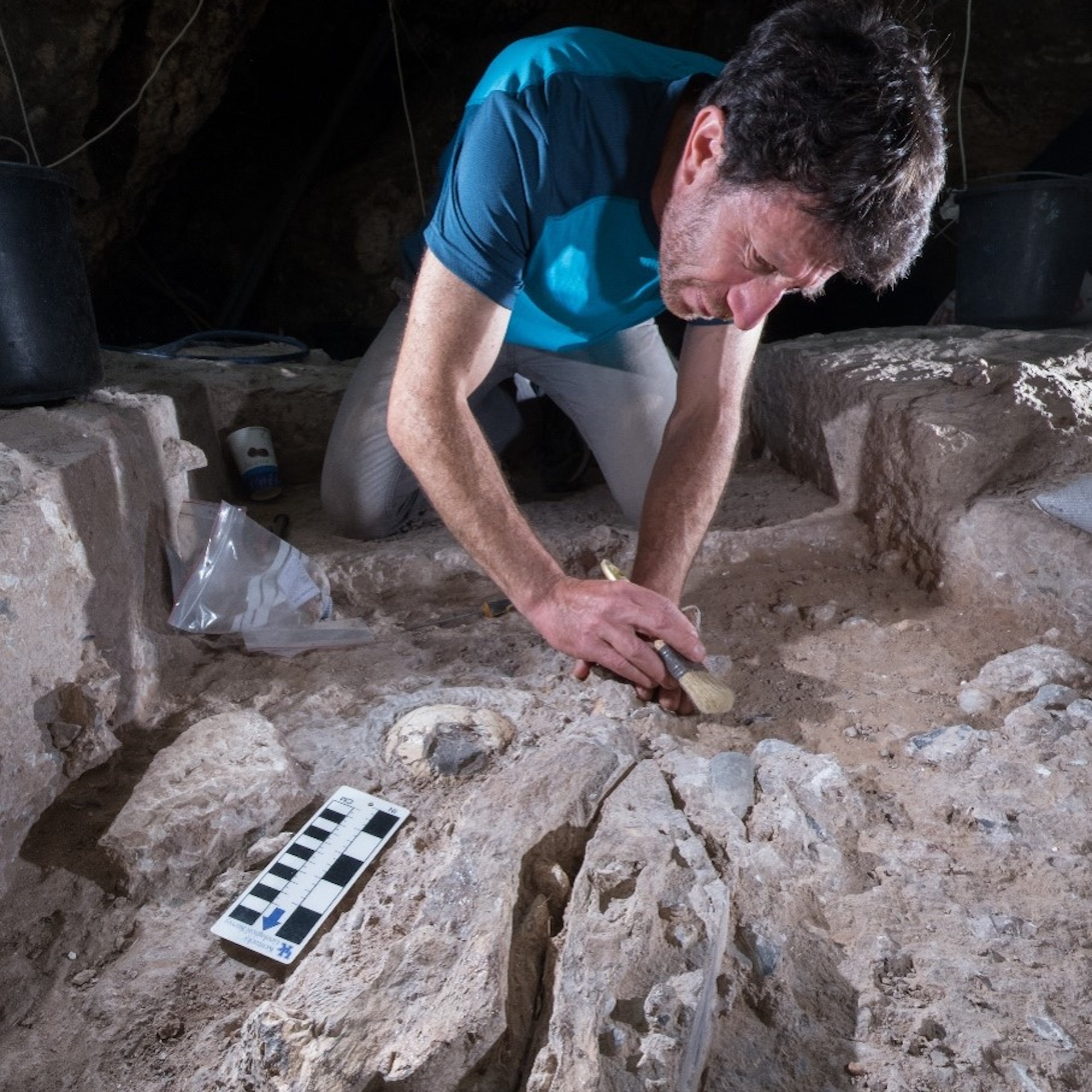 a man brushes away dirt in a cave excavation site