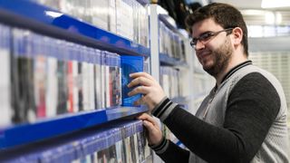 A man inspects a row of video game boxes with a smile on his face