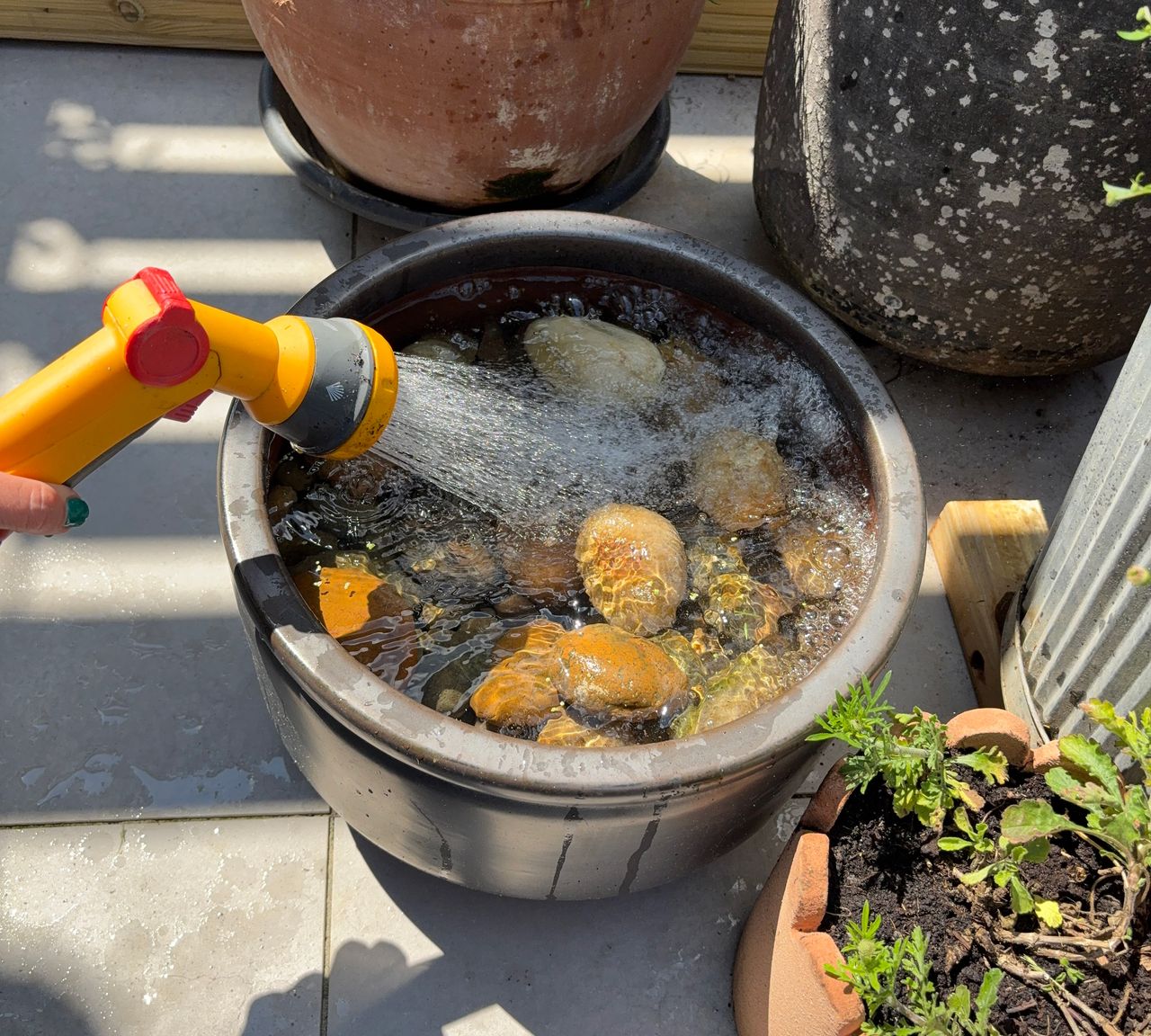 Grey ceramic planter on grey paved patio with hose spray filling it with water