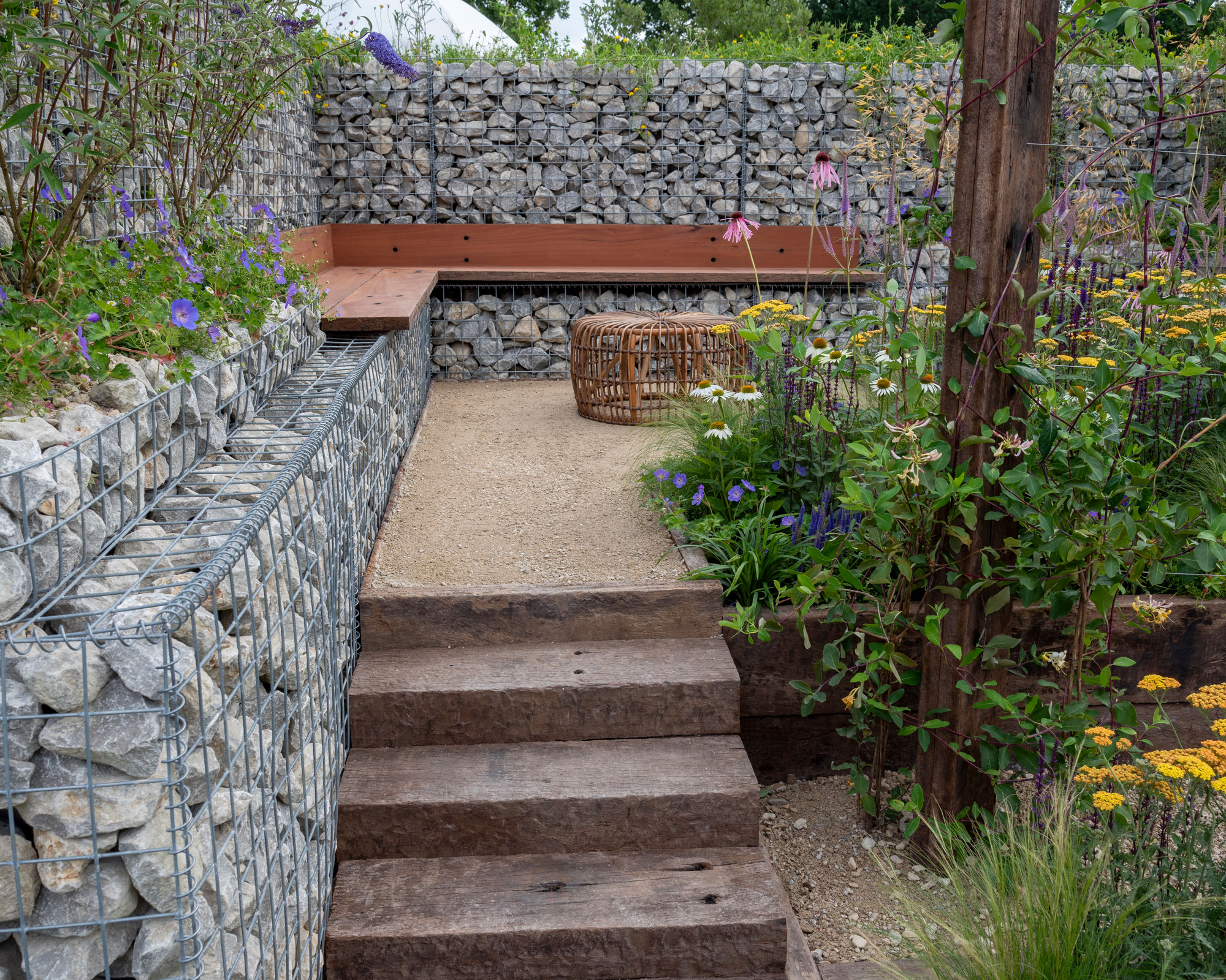 sloping garden with gabion walls and steps up to integrated bench, with flower planting in a bed