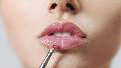 A woman applying lip gloss with a make-up brush, close-up of lips - stock photo