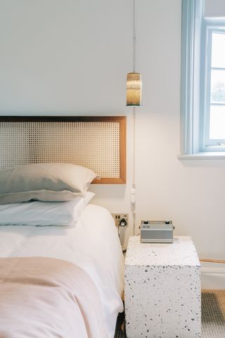 A bedroom with a bed, a wooden headboard, a marble side table and a wall lamp next to a window.