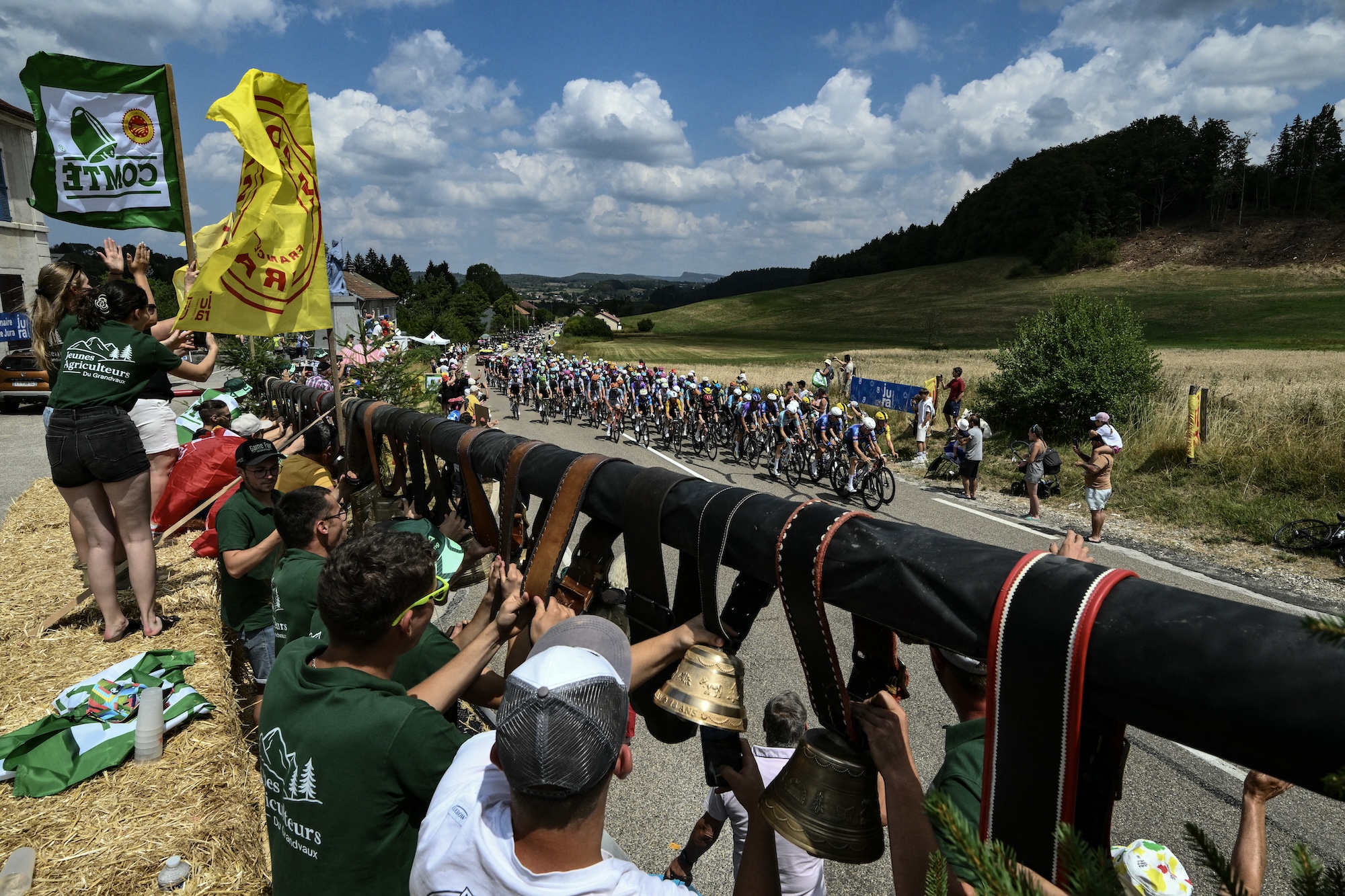 Spectators ring bells along the roadside as the pack of riders races by on stage 15