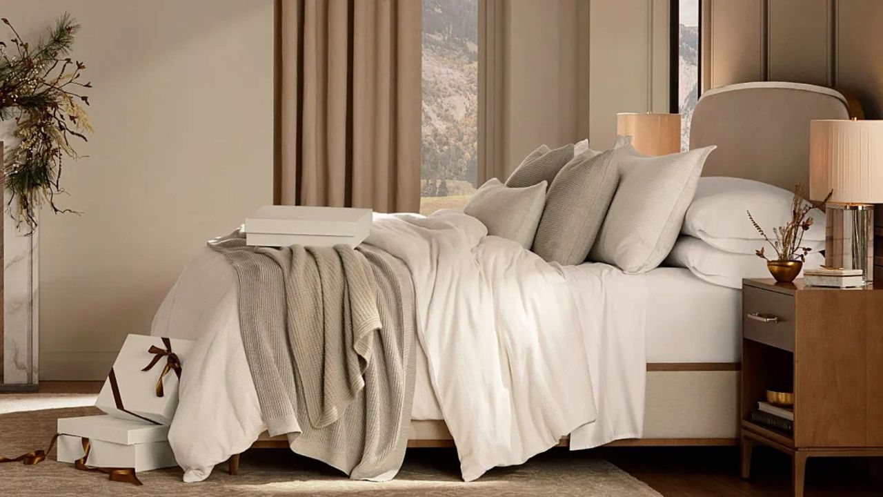 Side view of white bed sheets and comforter on a bed with beige pillows against a cream wall. 