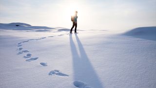 Young girl walks uphill through snow with the sun shining behind her as she ventures towards the unknown.