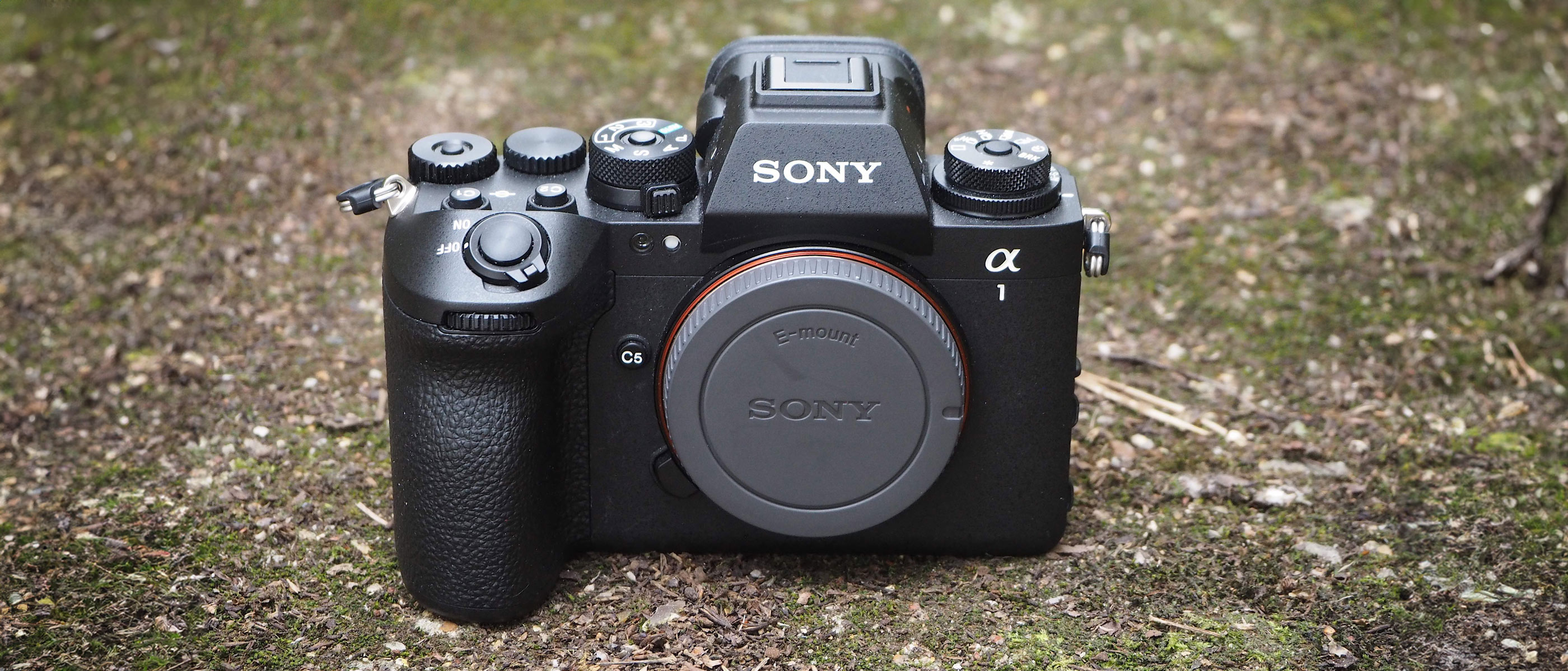 A Sony A1 II camera on the ground with moss in the background.