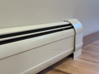 A white baseboard radiator against a white wall, on a wooden floor.