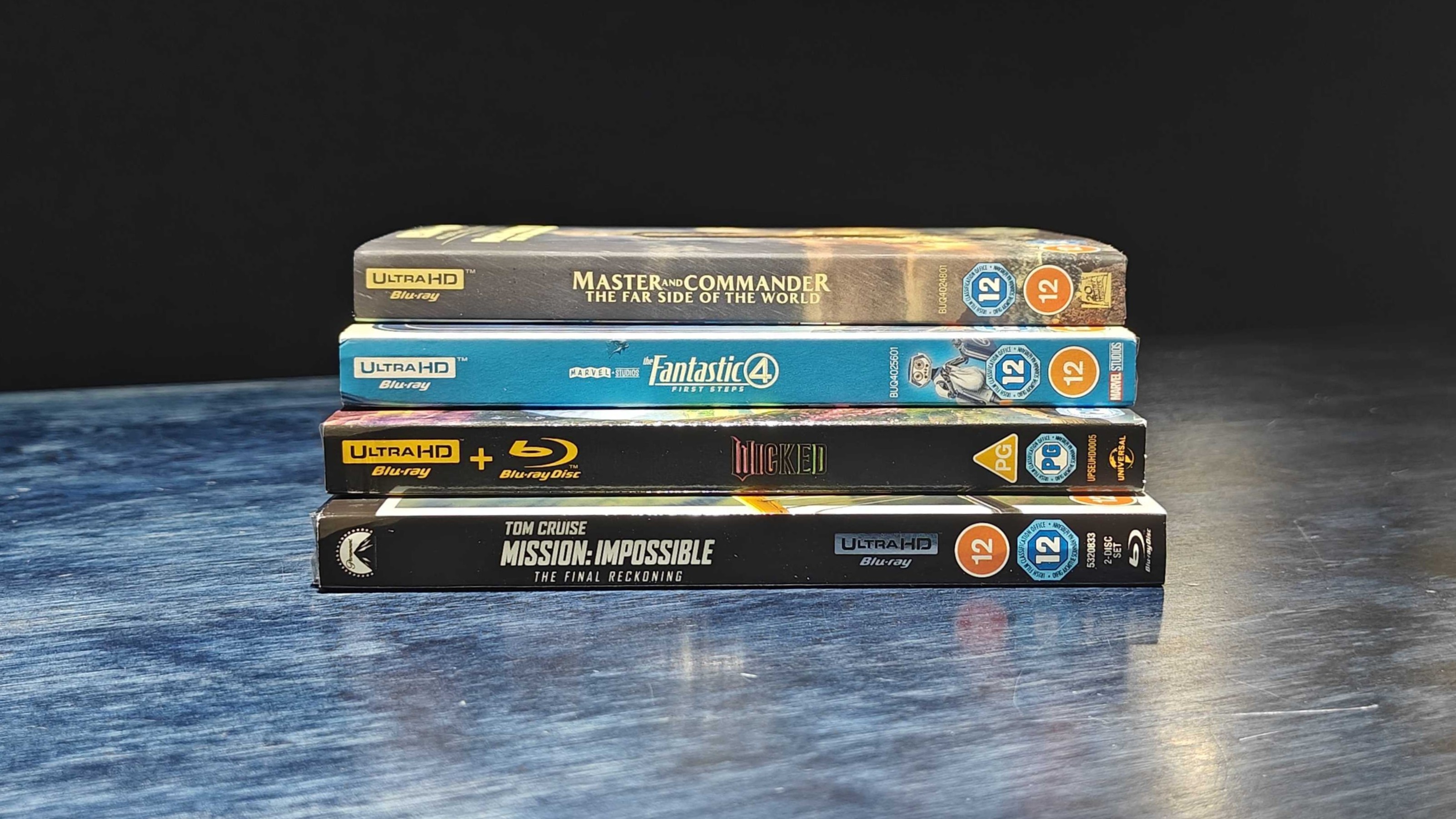 4K Blu-rays in a pile on a dark blue table.
