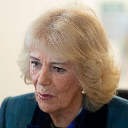 Queen Camilla wearing a teal coat and looking emotional