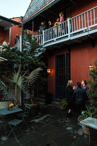 The inner courtyard of a New Orleans' hotel features terracotta and light blue balconies, plants, and mingling people.