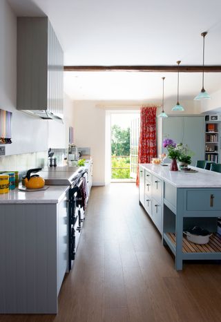 galley kitchen with grey-blue cabinets and island with door open to balcony and view outside and red curtains