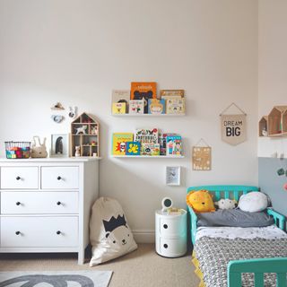 A children's room with a white IKEA chest of drawers, floating shelves displaying books, Kartell bedside table and a single turquoise bed