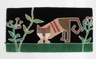 A rug with a cat standing on grass with flowers on it.