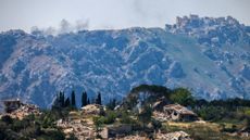 Destroyed buildings in the southern Lebanese village of Kfar Kila, with smoke rising in the distance behind the medieval Beaufort Castle, known locally as Qalaat al-Shaqif or Shaqif Arnoun, following an Israeli airstrike.
