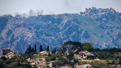 Destroyed buildings in the southern Lebanese village of Kfar Kila, with smoke rising in the distance behind the medieval Beaufort Castle, known locally as Qalaat al-Shaqif or Shaqif Arnoun, following an Israeli airstrike.