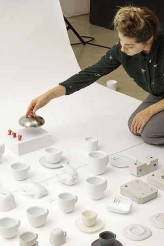 Federica Biasi kneeling on the floor on a white sheet with the ‘Lume’ collection of cups and saucers that were designed for Nespresso