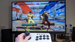 Hori Fighting Stick Mini being held in hand in front of monitor playing Street Fighter 6