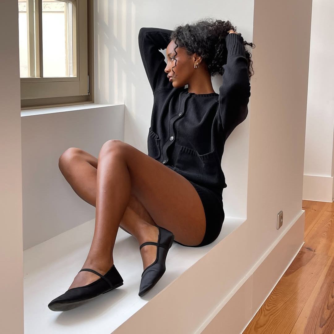 Rayan Xasan sits in a windowsill wearing a black lounge set and matching Mary Jane shoes