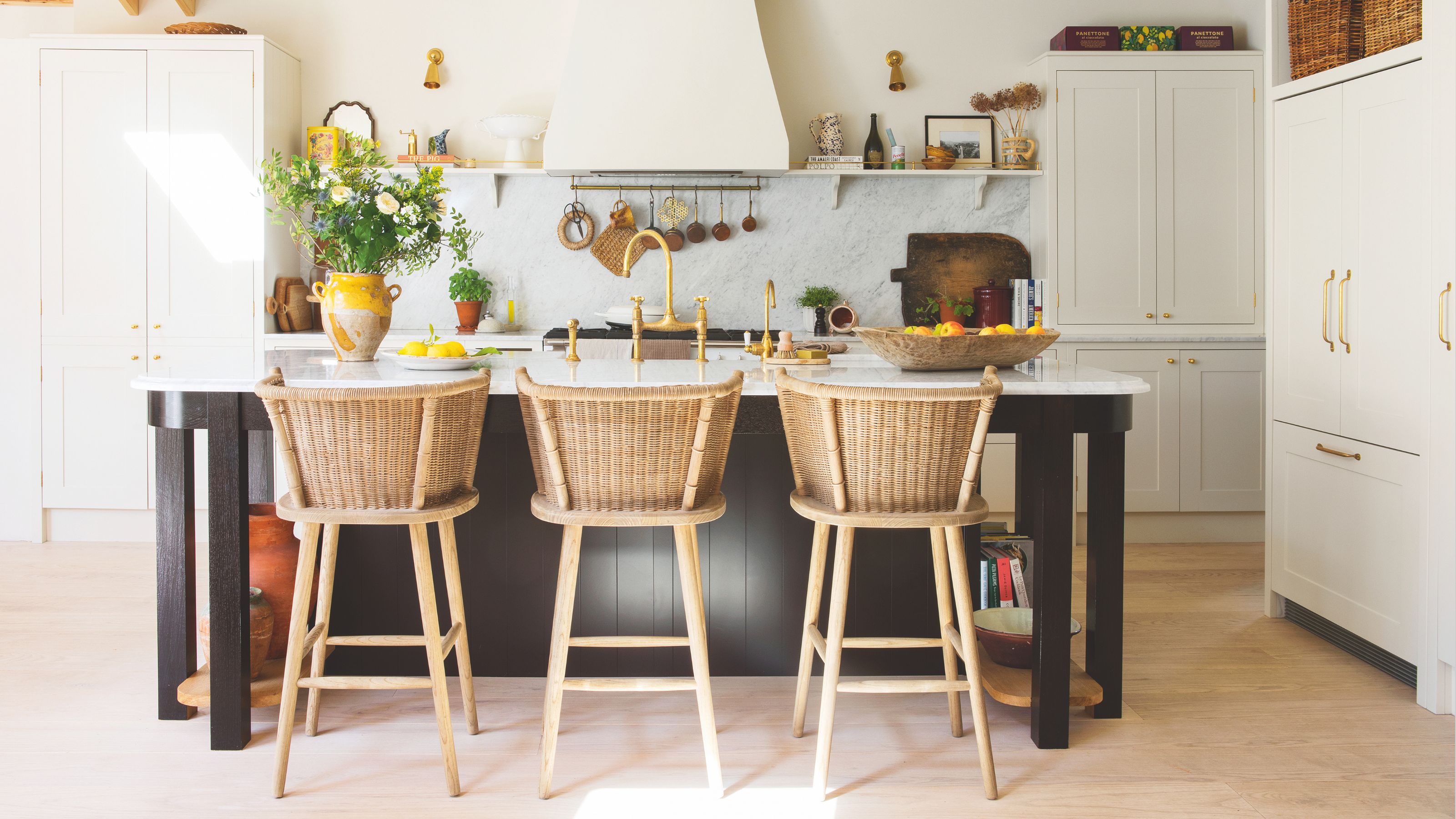 White kitchen with marble backsplash, black kitchen island with wicker stools around it