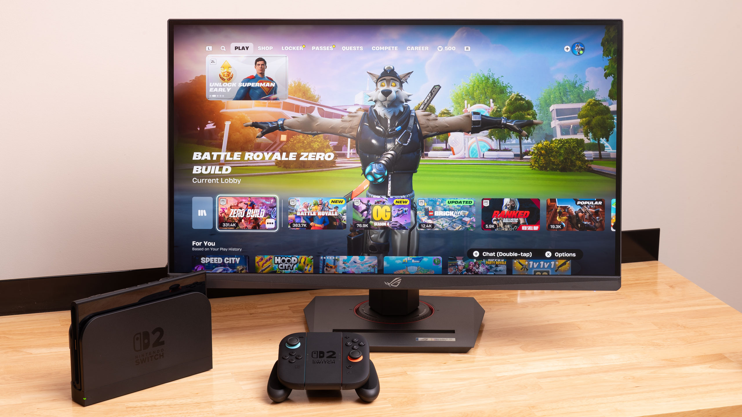 A docked Nintendo Switch 2 next to a gaming monitor with its controllers nearby