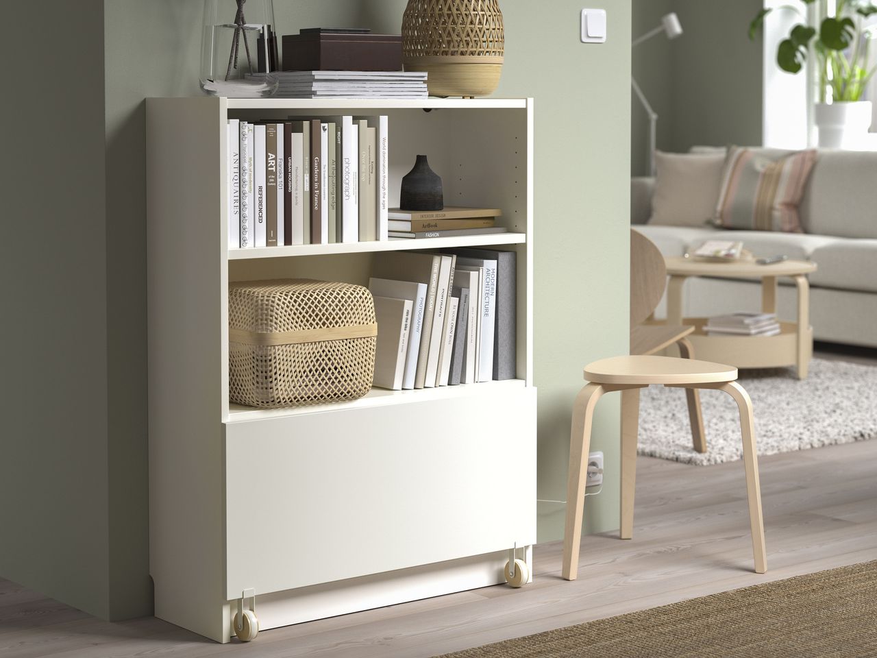 A living room with a small white bookcase against a wall with a pull out drawer with wheels at the bottom