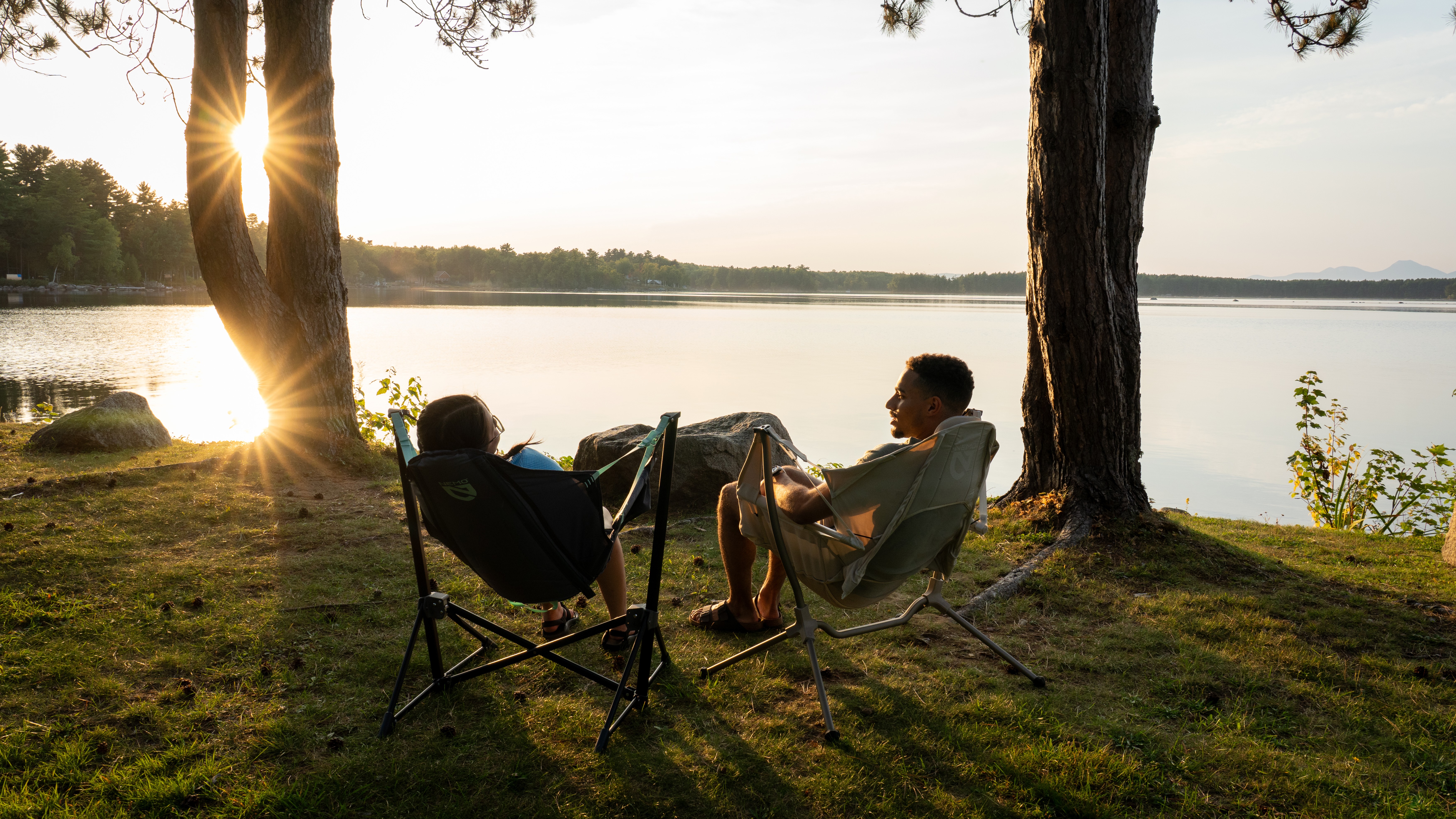 Two campers relaxing by a lake in the Nemo Stargaze Evo X camping chair