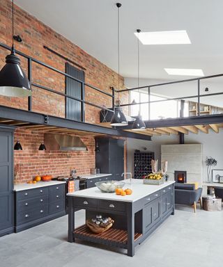 A black kitchen idea with exposed brick wall, black cabinetry and double height ceiling with raised walkway