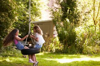 two girls playing on tire swing in garden