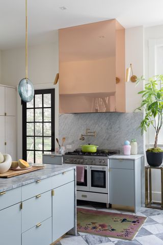 The kitchen sports pastel blue cabinets, painted floor tiles, a mirror acrylic hood surround and a pastel blue island light