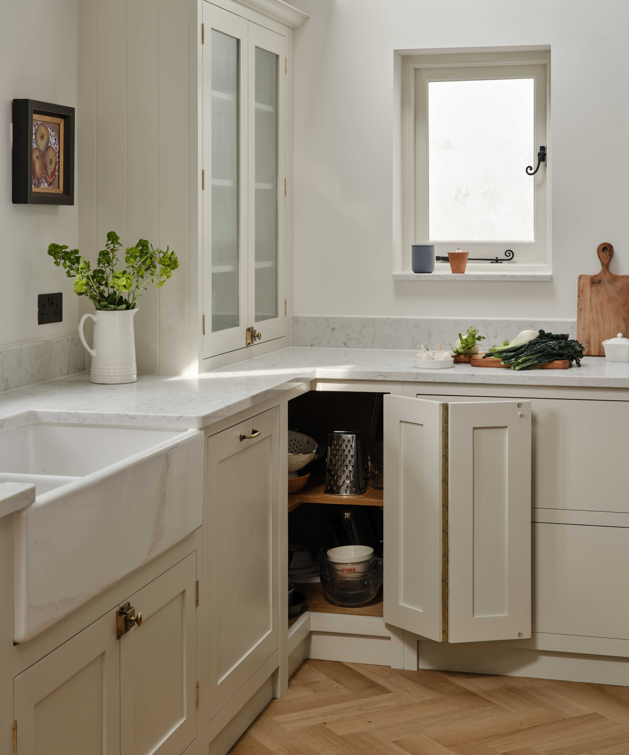 Cream shaker kitchen, Belfast sink, marble worktops and open bi-fold corner cupboard holding a grater and Pyrex bowls