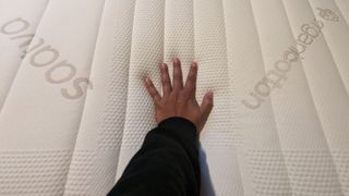 A hand pressing down on the Saatva Memory Foam Hybrid mattress