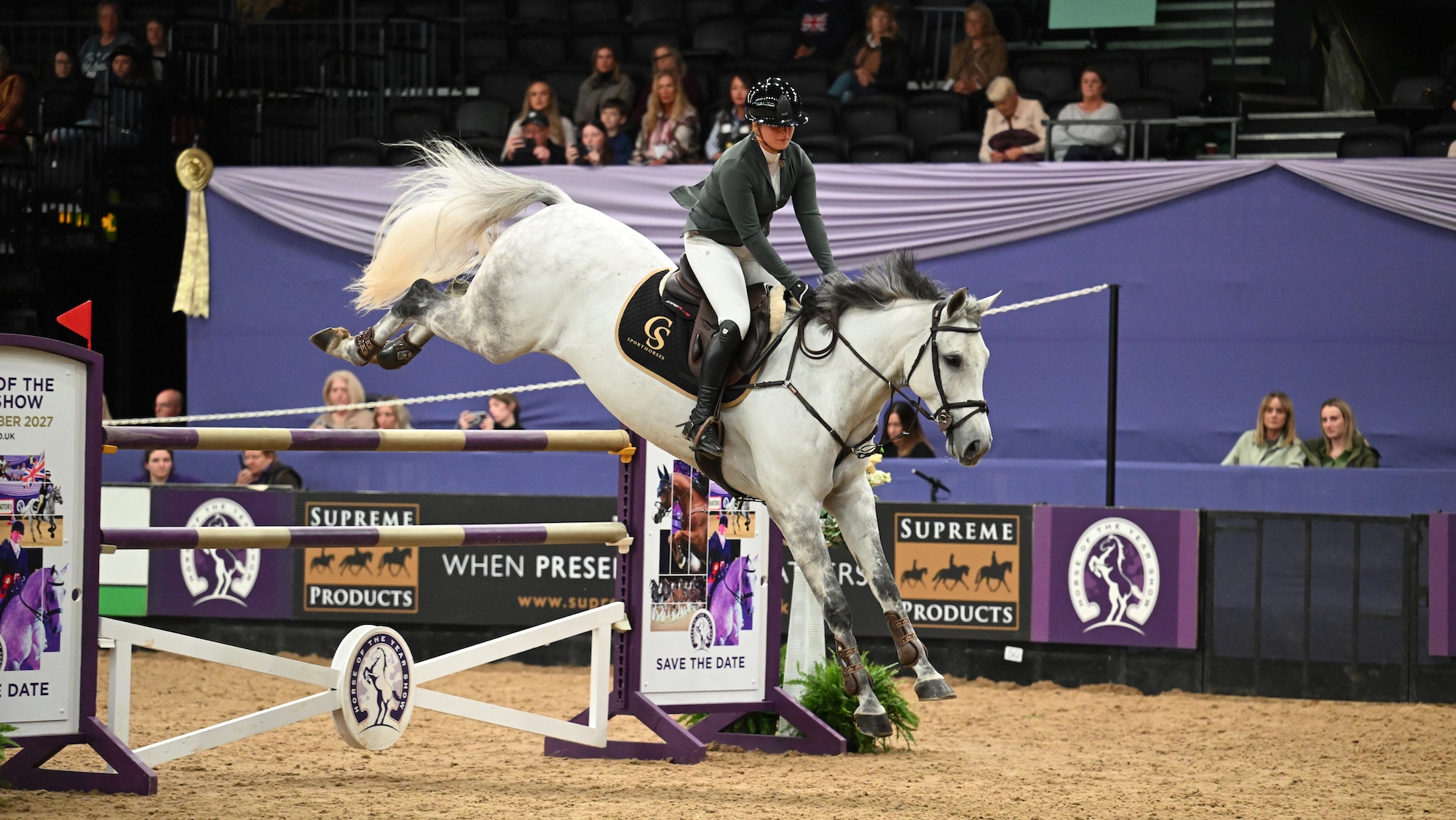 A rider and grey horse land over a vertical at HOYS